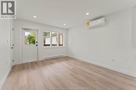 A spacious room with a door, a window, and a wall-mounted air conditioner unit.