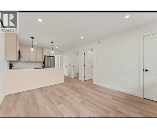 A spacious kitchen with light wood flooring and white walls.