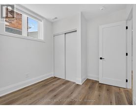 A room with white walls and wooden flooring, with a window showing a brick building outside.