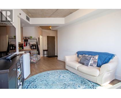 A living room with a couch and a kitchen area in the background.