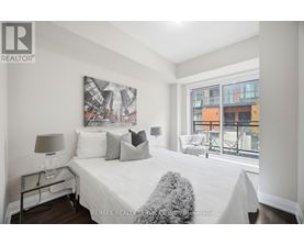 A bedroom with a large bed, a nightstand with a lamp, and a picture on the wall.