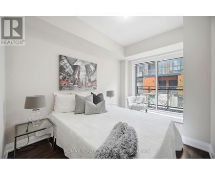 A bedroom with a large bed, a nightstand with a lamp, and a picture on the wall.