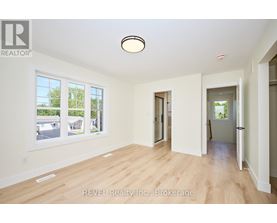 A spacious room with wooden flooring and white walls, with a large window on the left side.