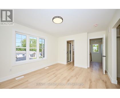 A spacious room with wooden flooring and white walls, with a large window on the left side.