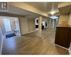 A real estate listing photo of a spacious room with wood flooring and white walls.