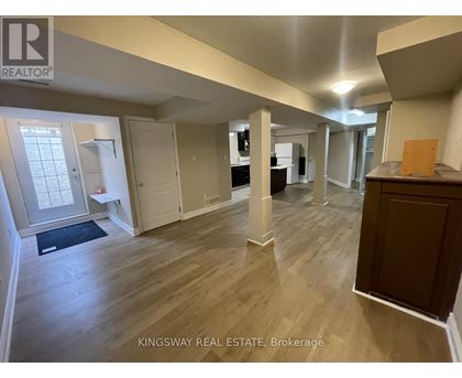 A real estate listing photo of a spacious room with wood flooring and white walls.