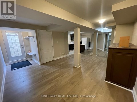 A real estate listing photo of a spacious room with wood flooring and white walls.