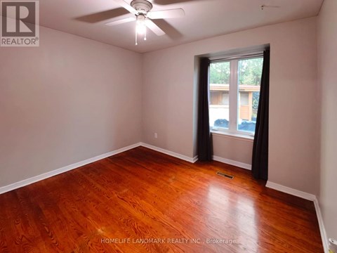 A room with a ceiling fan and a window with a view of trees.