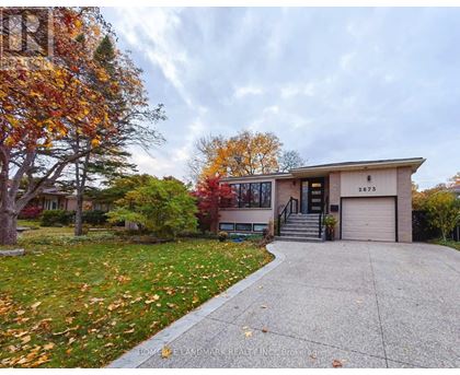 A house with a driveway and a tree with orange leaves.