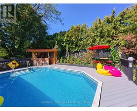 A pool surrounded by trees and a deck with a hot tub.