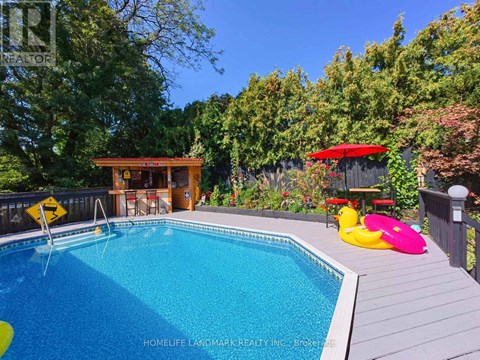 A pool surrounded by trees and a deck with a hot tub.