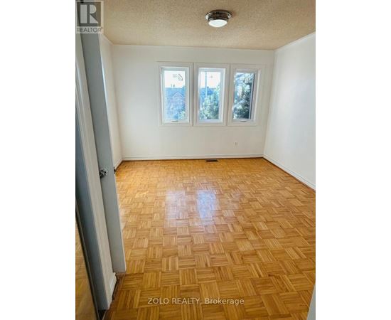 A room with wooden flooring and a window showing a view of trees.