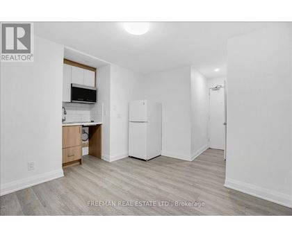 A white kitchen with a refrigerator, cabinets, and a microwave.