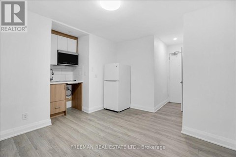 A white kitchen with a refrigerator, cabinets, and a microwave.
