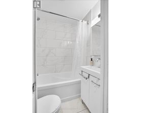 A white bathroom with a marble tile wall and a glass shower door.