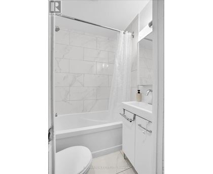 A white bathroom with a marble tile wall and a glass shower door.