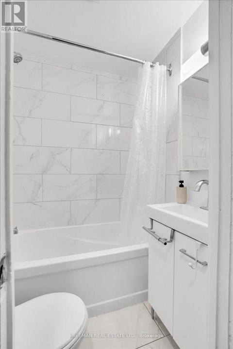 A white bathroom with a marble tile wall and a glass shower door.