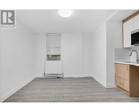 A white room with a wooden floor and a small kitchenette.
