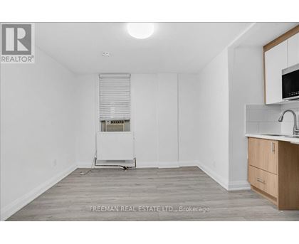 A white room with a wooden floor and a small kitchenette.