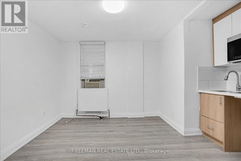A white room with a wooden floor and a small kitchenette.