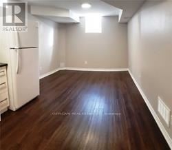 A room with wooden flooring and a white refrigerator.