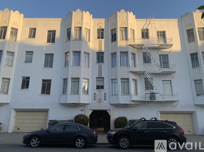 Two cars are parked in front of a white building with a balcony.