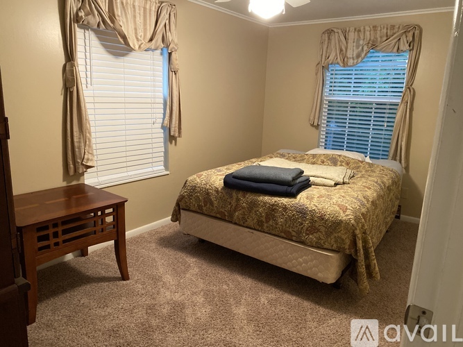 A bedroom with a bed, a nightstand, and a window with curtains.