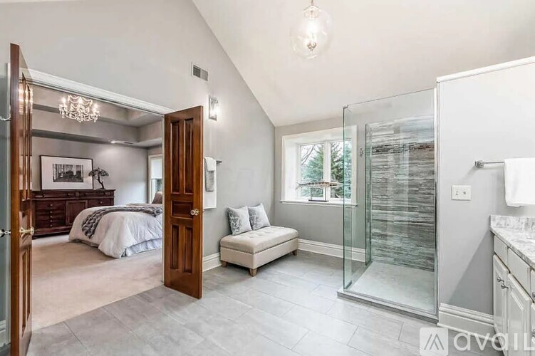 A bedroom with a bed, a bench, and a shower with a glass door.