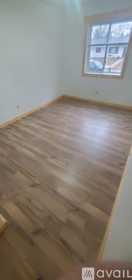 A room with wooden flooring and a window showing a building outside.