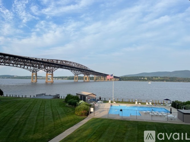 A bridge spans across a body of water with a pool and lawn in the foreground.