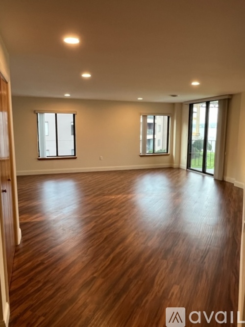 A spacious room with wooden flooring and large windows.