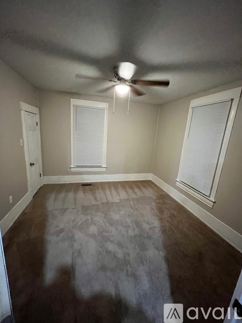 A room with a ceiling fan and two windows.