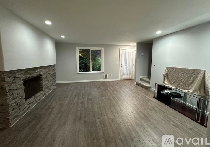 A spacious living room with wood flooring and a stone fireplace.