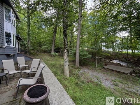 A patio with chairs and a table is surrounded by trees.