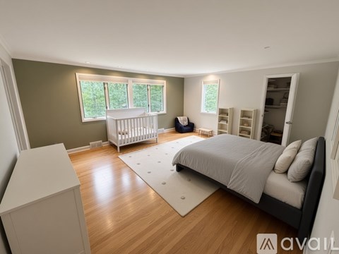 A baby's crib sits in a well-lit bedroom with a large bed and a dresser.