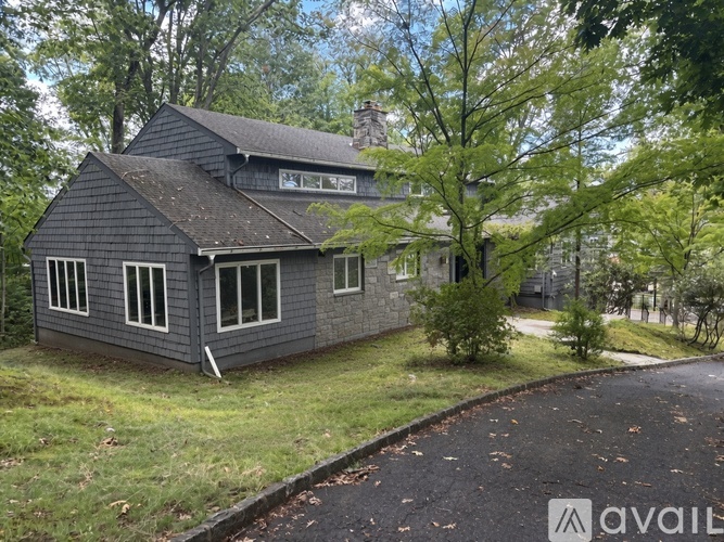 A house with a grey exterior is surrounded by trees and has a driveway leading to the front door.