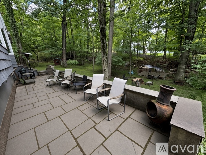 A patio with chairs and a table surrounded by trees.