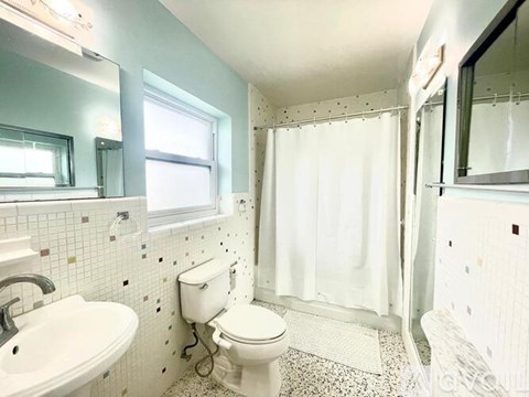 A white toilet sits in a bathroom with a white sink and a shower curtain.