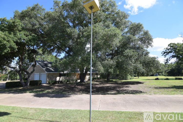 A pole with a yellow box on top stands in a grassy area with trees and a house in the background.