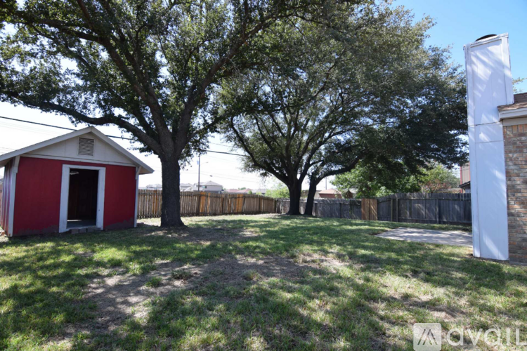 A red and white building sits in a yard with a tree in front of it.