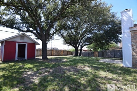 A red and white building sits in a yard with a tree in front of it.