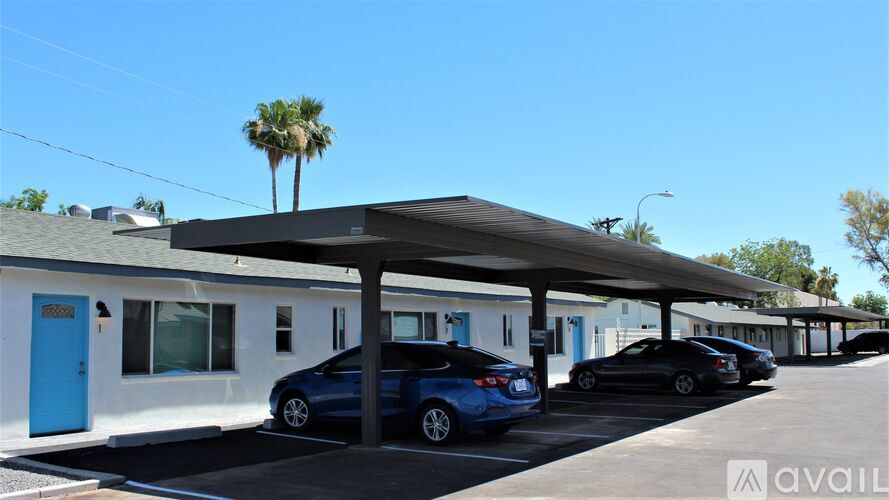 A row of small white buildings with blue doors and a carport with cars parked under it.