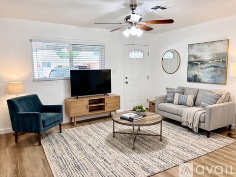 A living room with a blue chair, a coffee table, a couch, a television, and a painting on the wall.