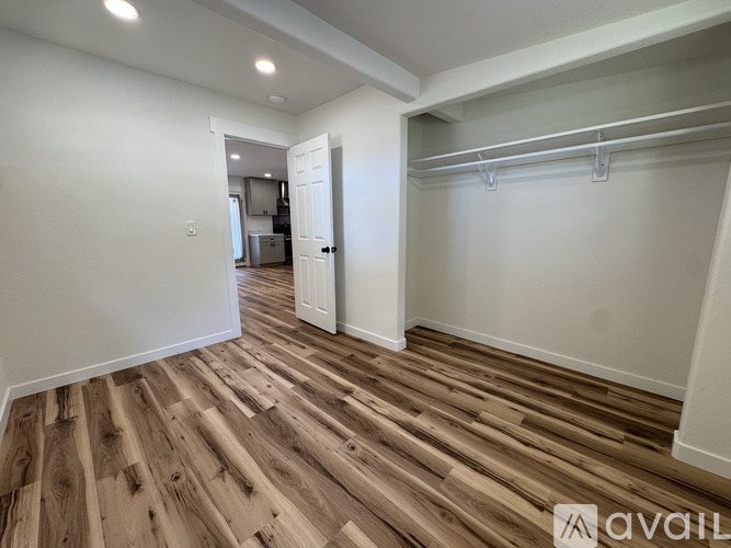 A room with wooden flooring and white walls, with a door leading to another room.