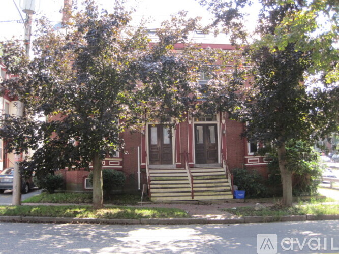 A red brick house with a porch and a tree in front.