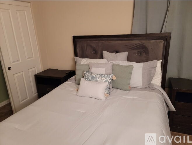 A bed with a white comforter and four pillows with a brown headboard.