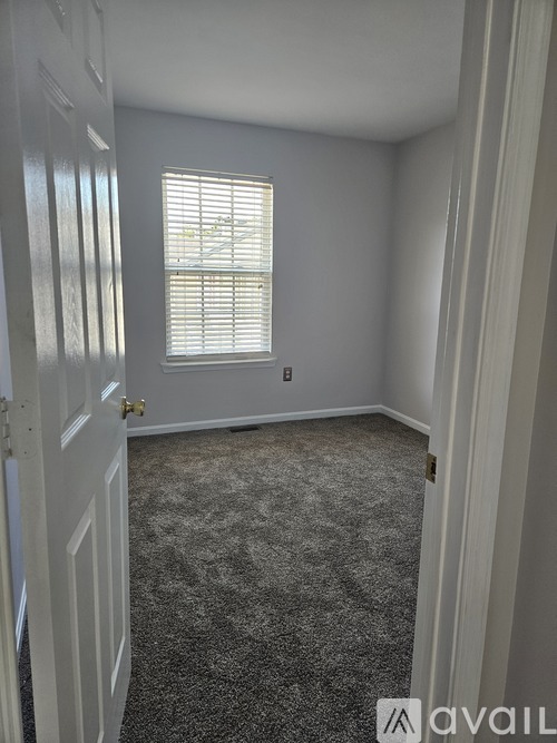 A carpeted room with a window and a door.
