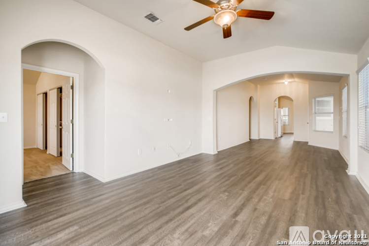 A spacious room with wood flooring and a ceiling fan.