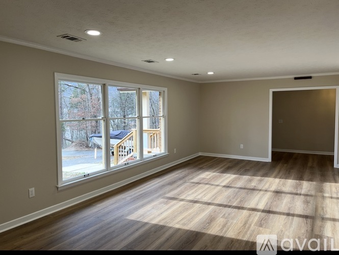 A spacious room with wooden flooring and a large window overlooking a residential area.