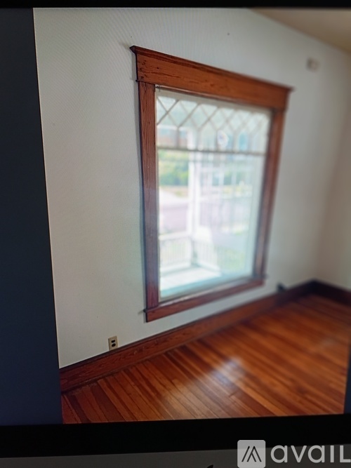 A window with a view of a balcony is in a room with wooden floors.